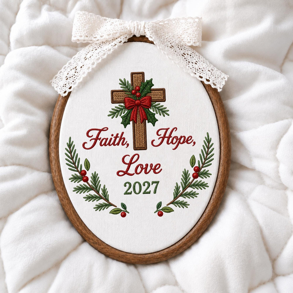 May include: An oval embroidery hoop frame containing white fabric with a stitched brown cross, green holly leaves, red berries, and a red bow. The text reads Faith, Hope, Love and 2027. A white lace ribbon is tied in a bow at the top of the frame.