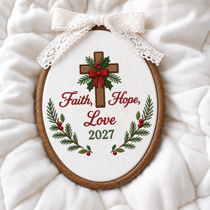 May include: An oval embroidery hoop frame containing white fabric with a stitched brown cross, green holly leaves, red berries, and a red bow. The text reads Faith, Hope, Love and 2027. A white lace ribbon is tied in a bow at the top of the frame.