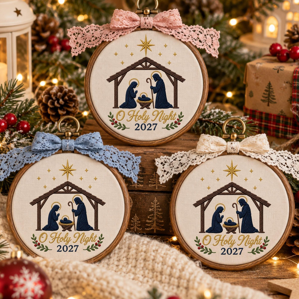 May include: Three circular wooden embroidery hoops featuring a nativity scene with a stable, figures, and a star. Each hoop is topped with a lace bow in pink, blue, or cream. The text O Holy Night 2027 is embroidered in brown on cream fabric.