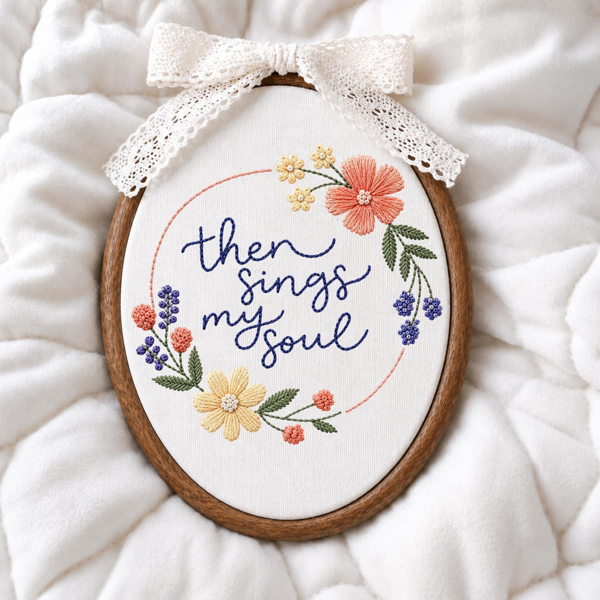 May include: An oval wooden embroidery hoop containing white fabric with the hand-stitched dark blue text then sings my soul. The text is surrounded by a circular floral wreath featuring yellow, coral, and purple flowers with green leaves and a white lace bow.